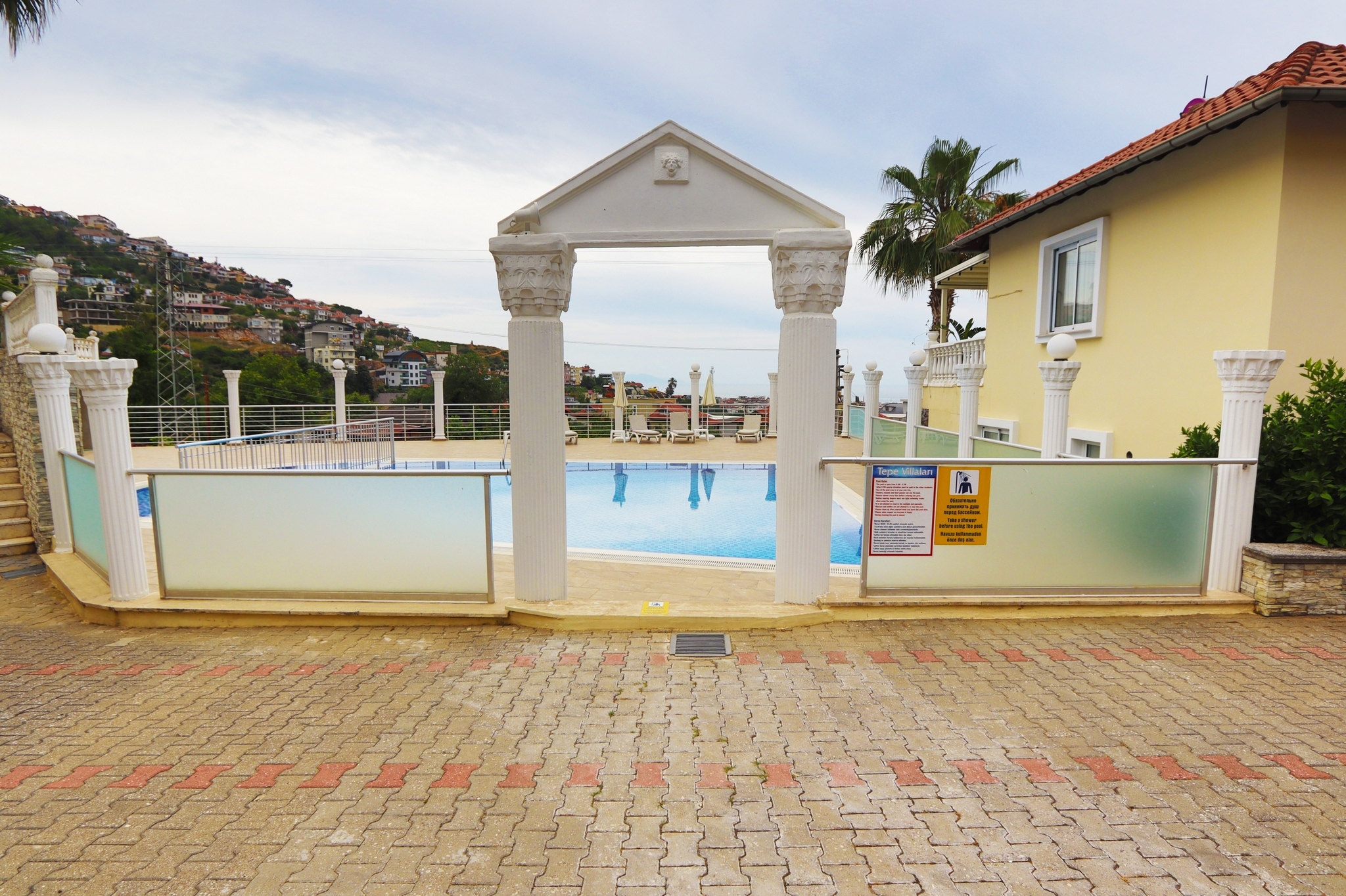 Outdoor pool behind glass fencing with loungers, a stone arch and sea in the background