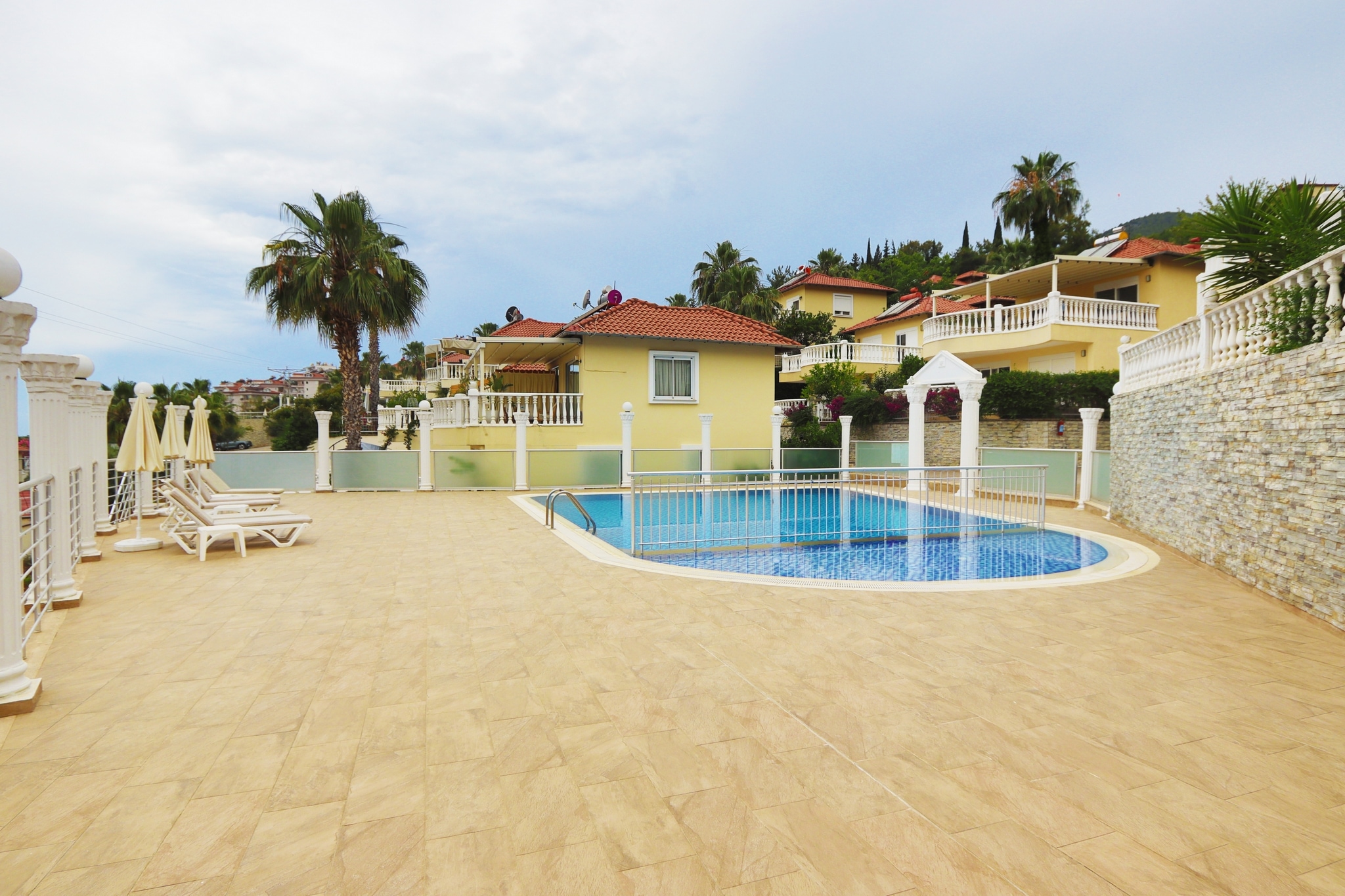 Oval outdoor pool with loungers and umbrellas beside villas for sale in Turkey