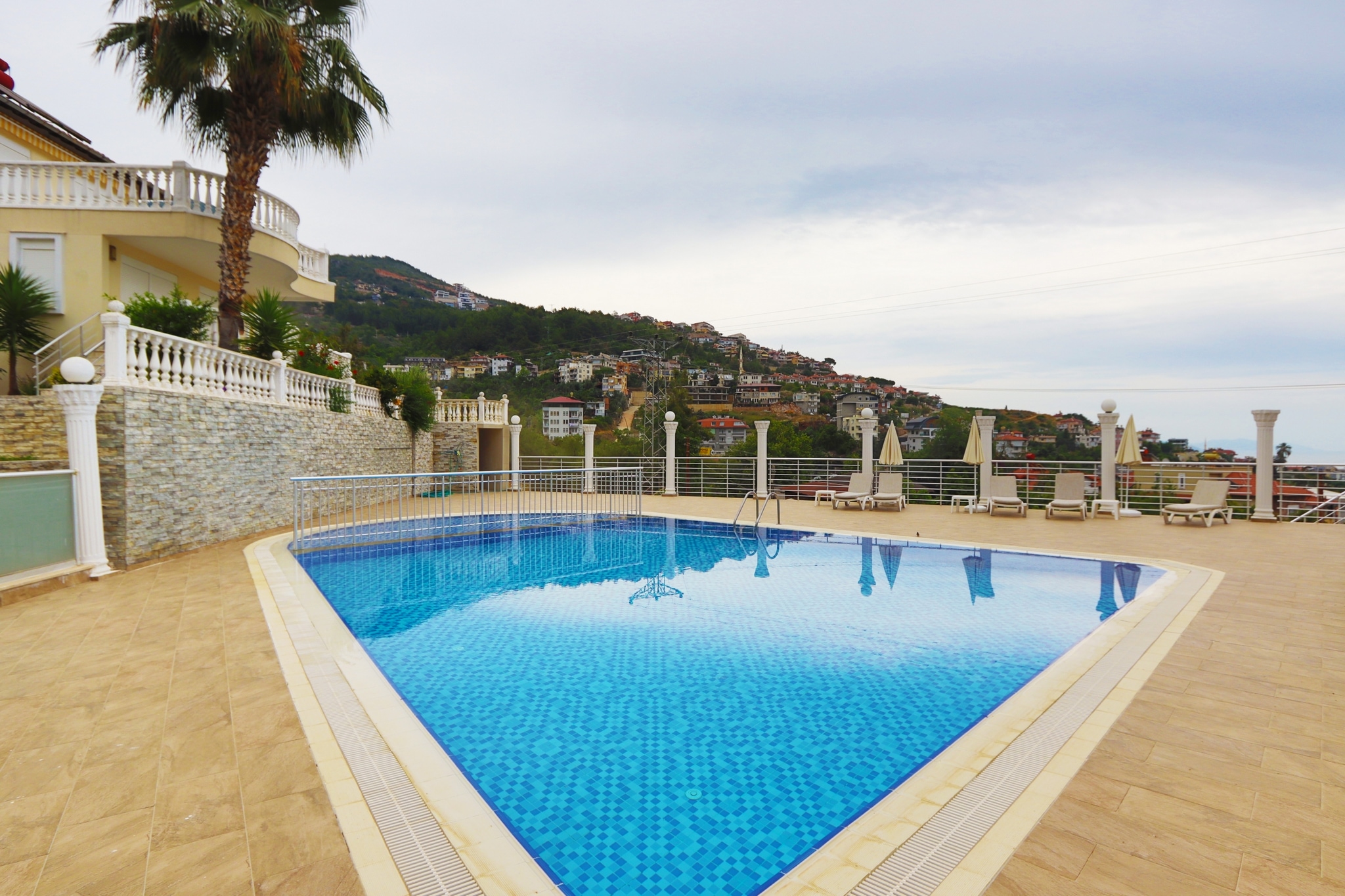 Outdoor pool with blue mosaic finish, loungers and sea beyond, where homes are for sale in Alanya