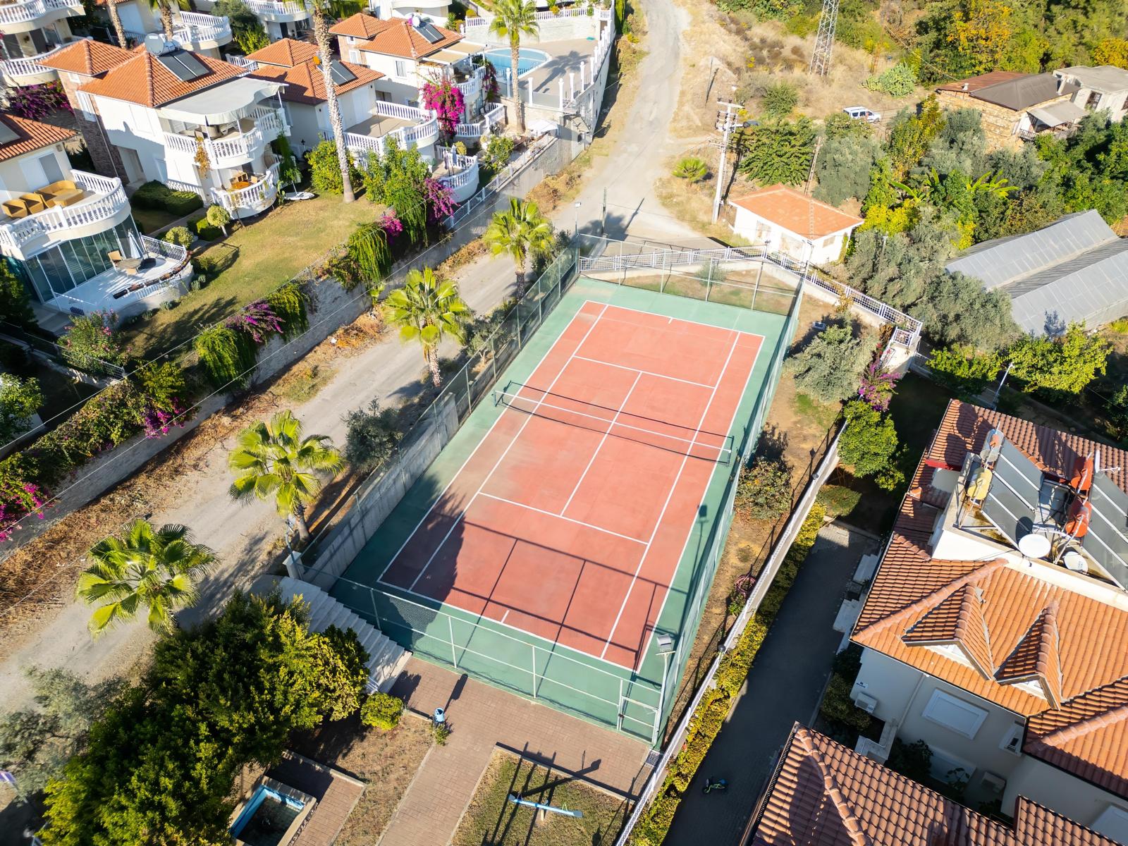Outdoor tennis court with mesh fencing, palms and red-roofed villas in Alanya