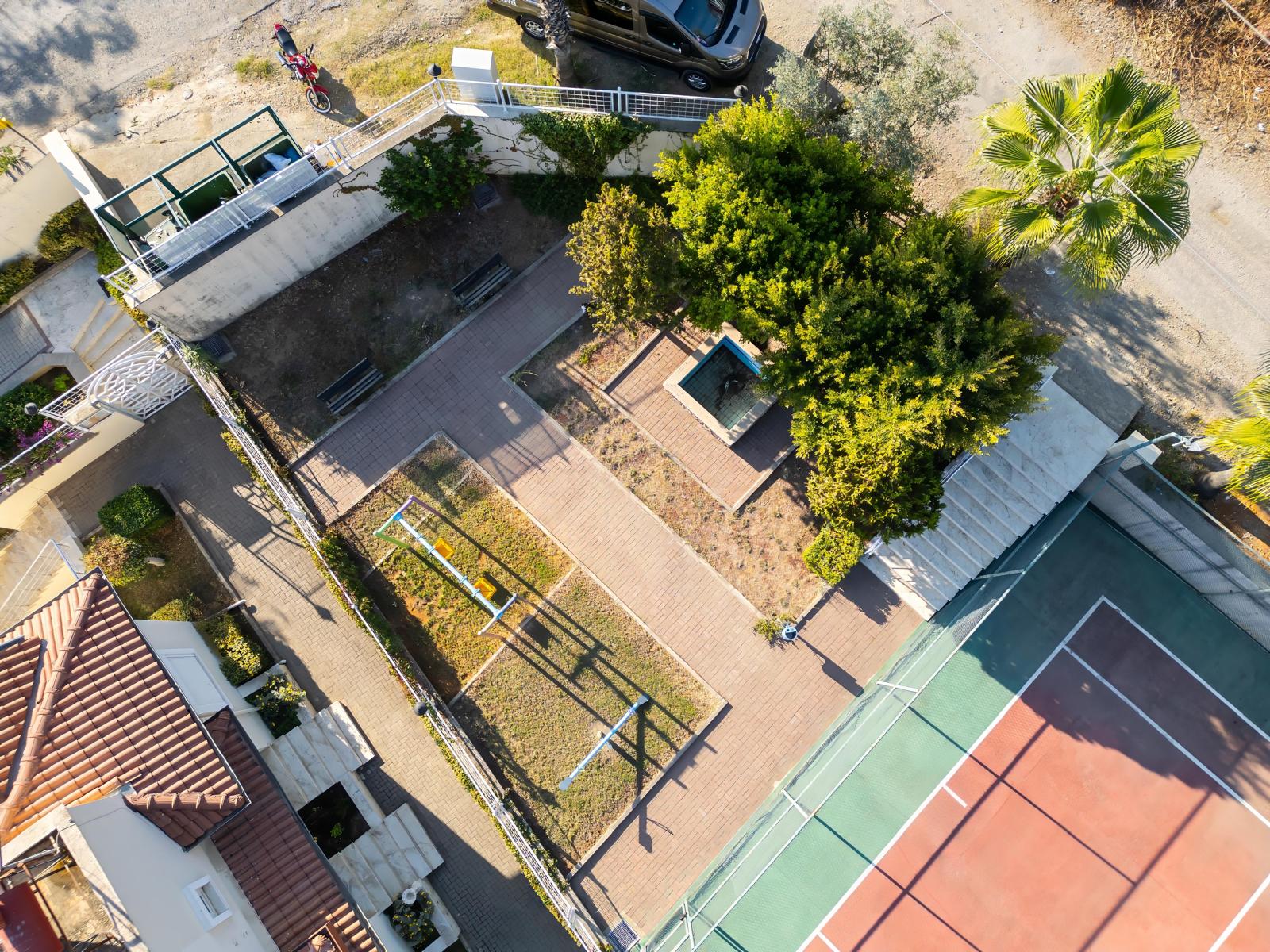Children’s playground with a yellow and blue slide, wooden path and part of a tennis court by a villa