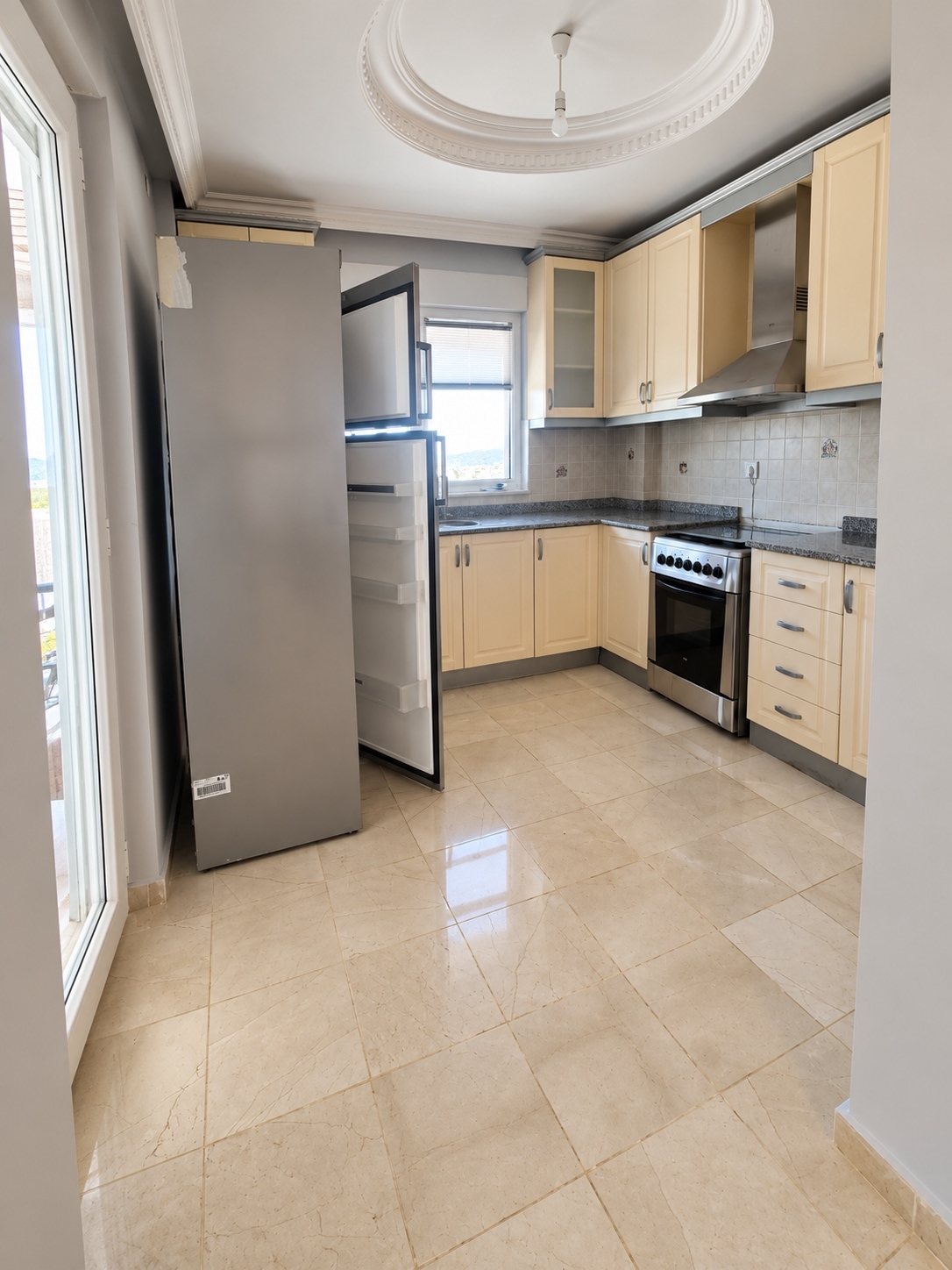 Corner kitchen with paneled light cabinets and gray stone counters in Alanya
