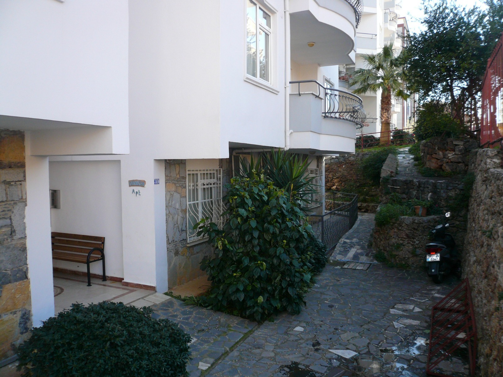 A stone path with red railings beside an apartment complex where apartments are for sale