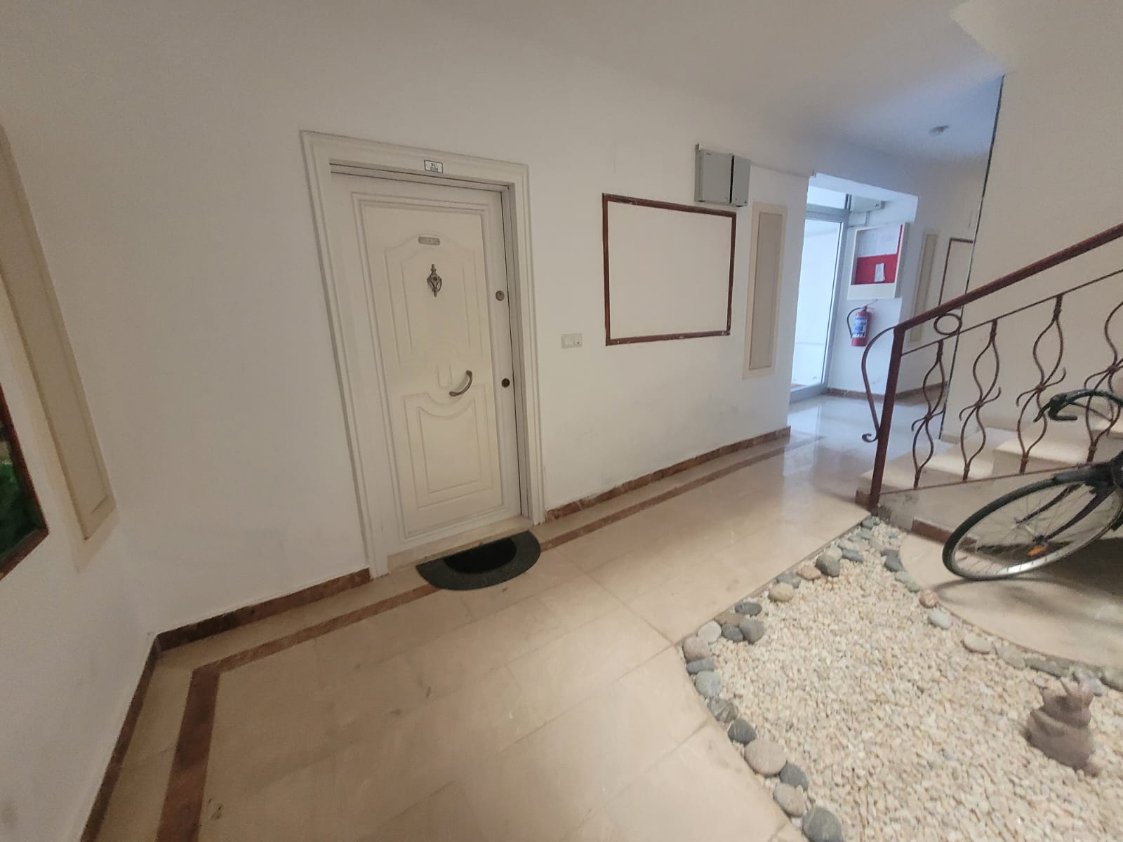 Apartment entrance door beside white pebbles and a wrought-iron stair rail in the hall