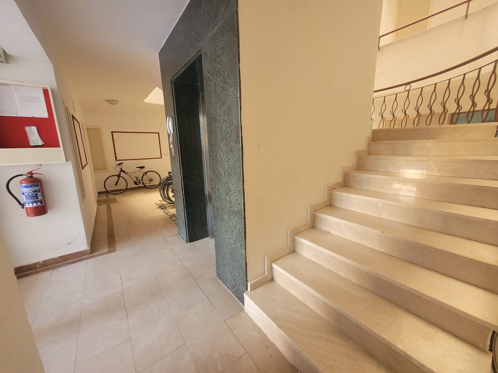 Marble staircase with wave-pattern wrought-iron rails and an announcement board in Tosmur
