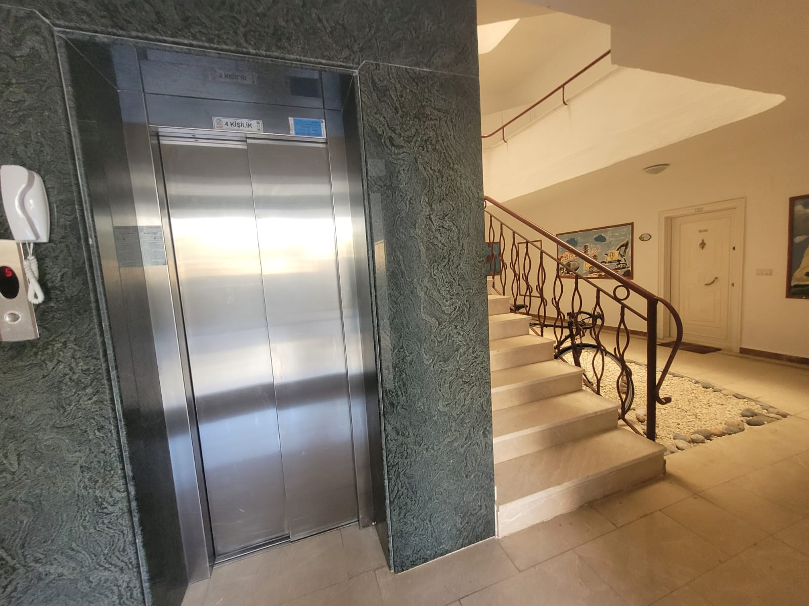 Elevator doors beside a marble staircase with wrought-iron rails in an apartment hall
