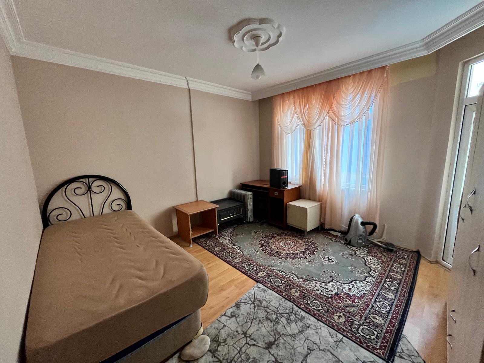 Bedroom with a single bed, corner sofa and TV beside a patterned rug in an apartment