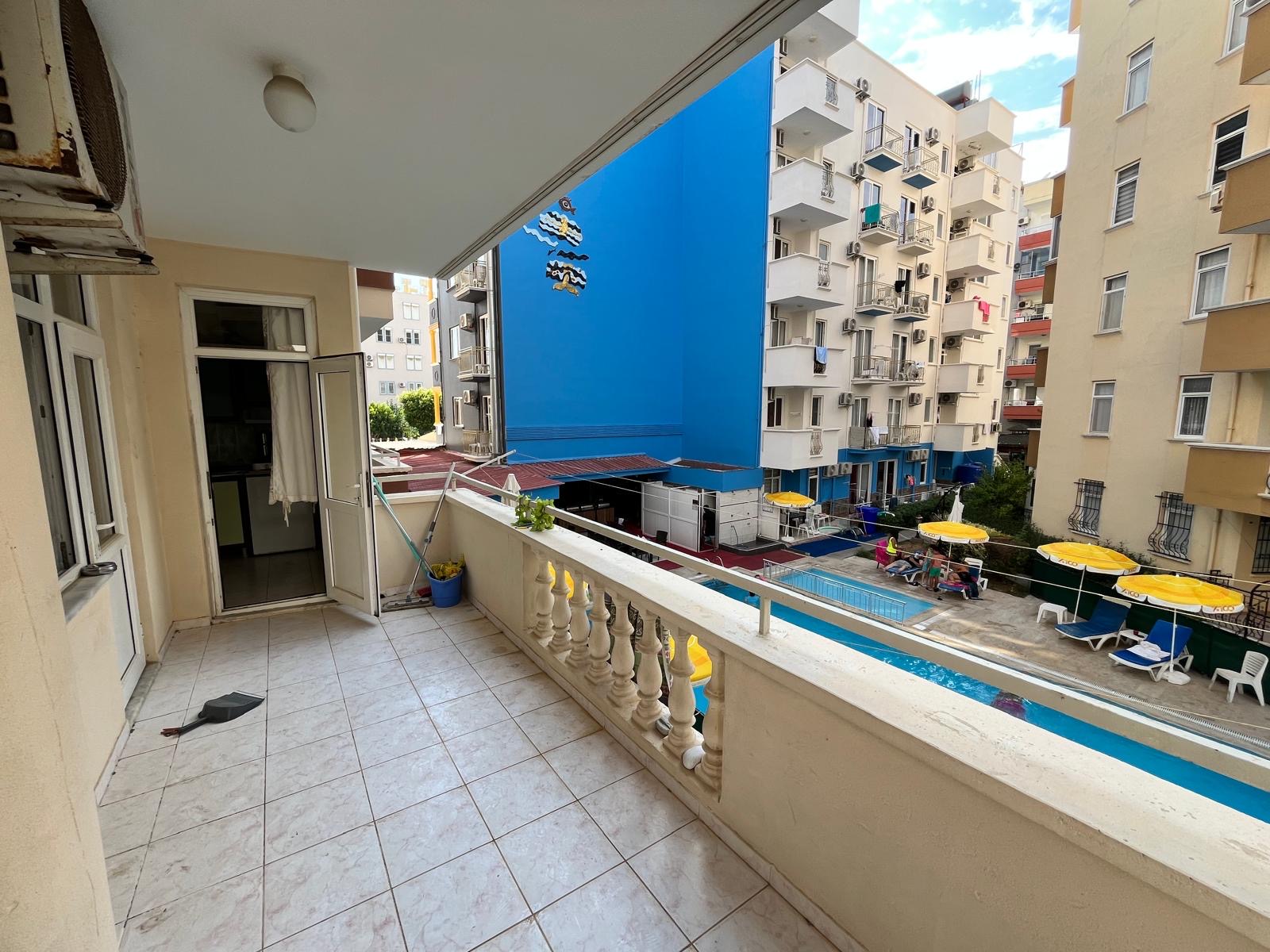 A covered balcony with a balustrade overlooks a pool with yellow umbrellas in a flat in Turkey
