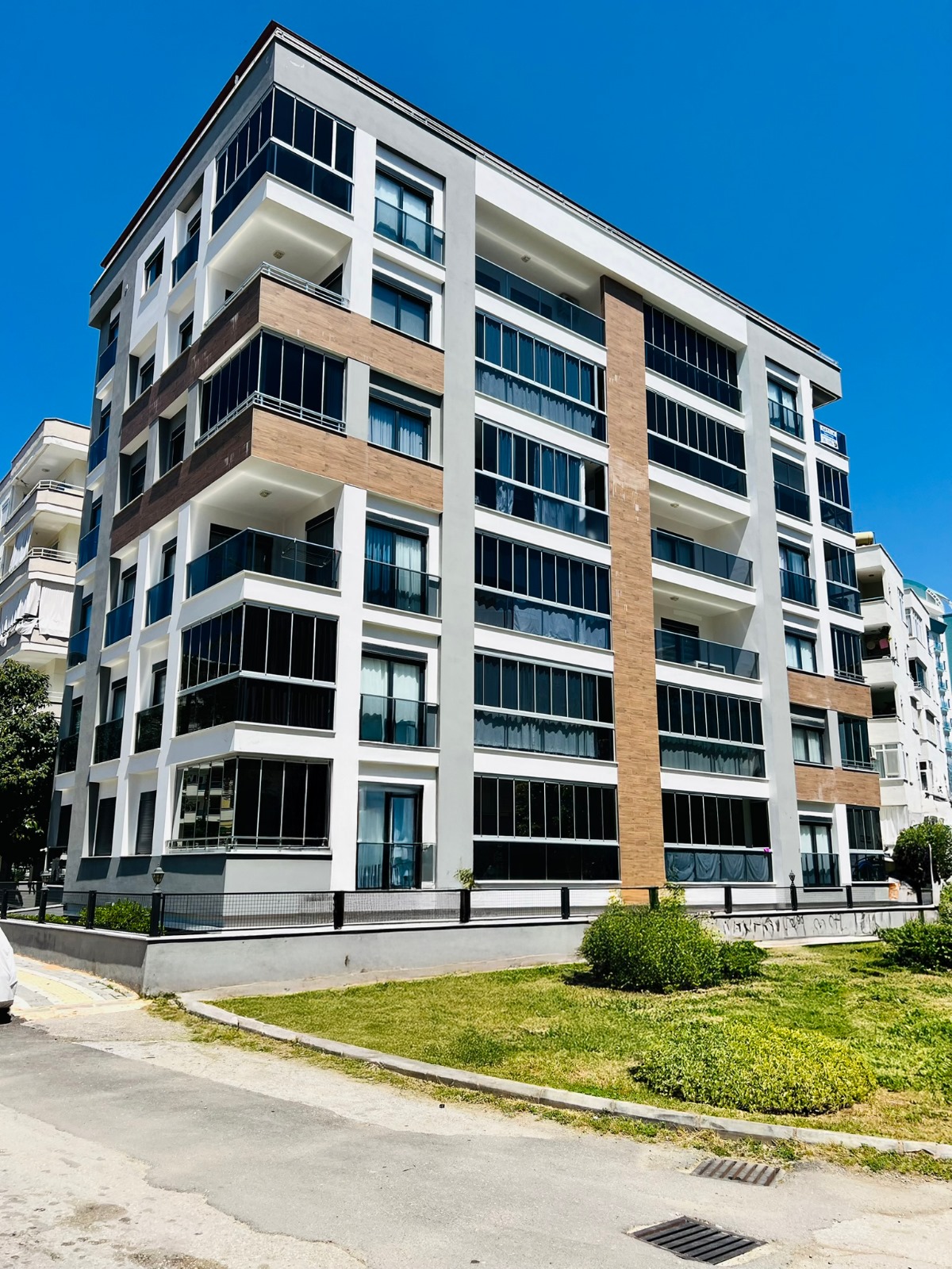 Panoramik camlı köşe bina cephesi önündeki çim alanla Türkiye’de satılık rezidansı gösteriyor