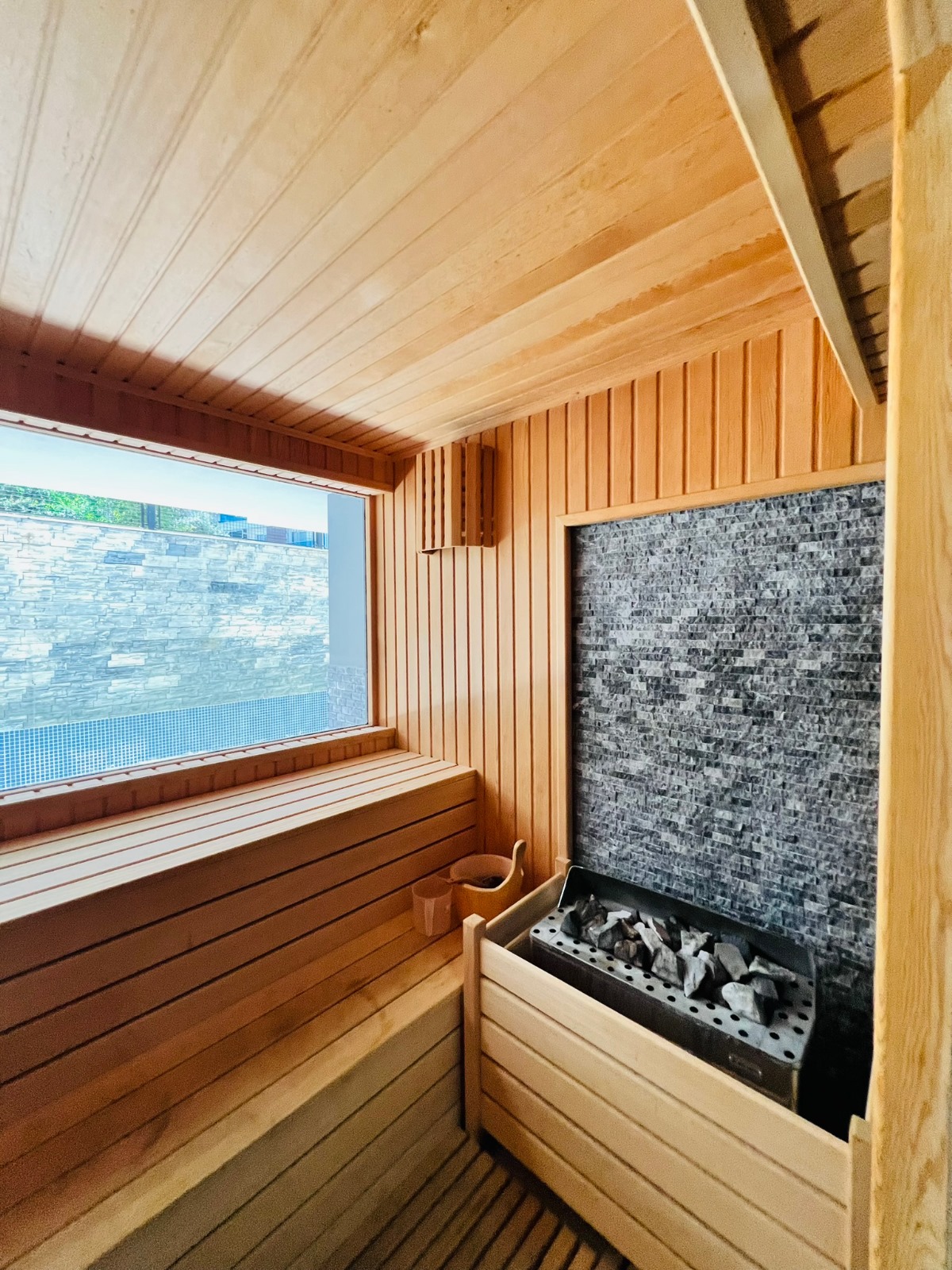 Pencereli sauna, taşlı sobasıyla havuz ve taş duvar manzarasına sahip çatı katı dairelerin kompleksinde