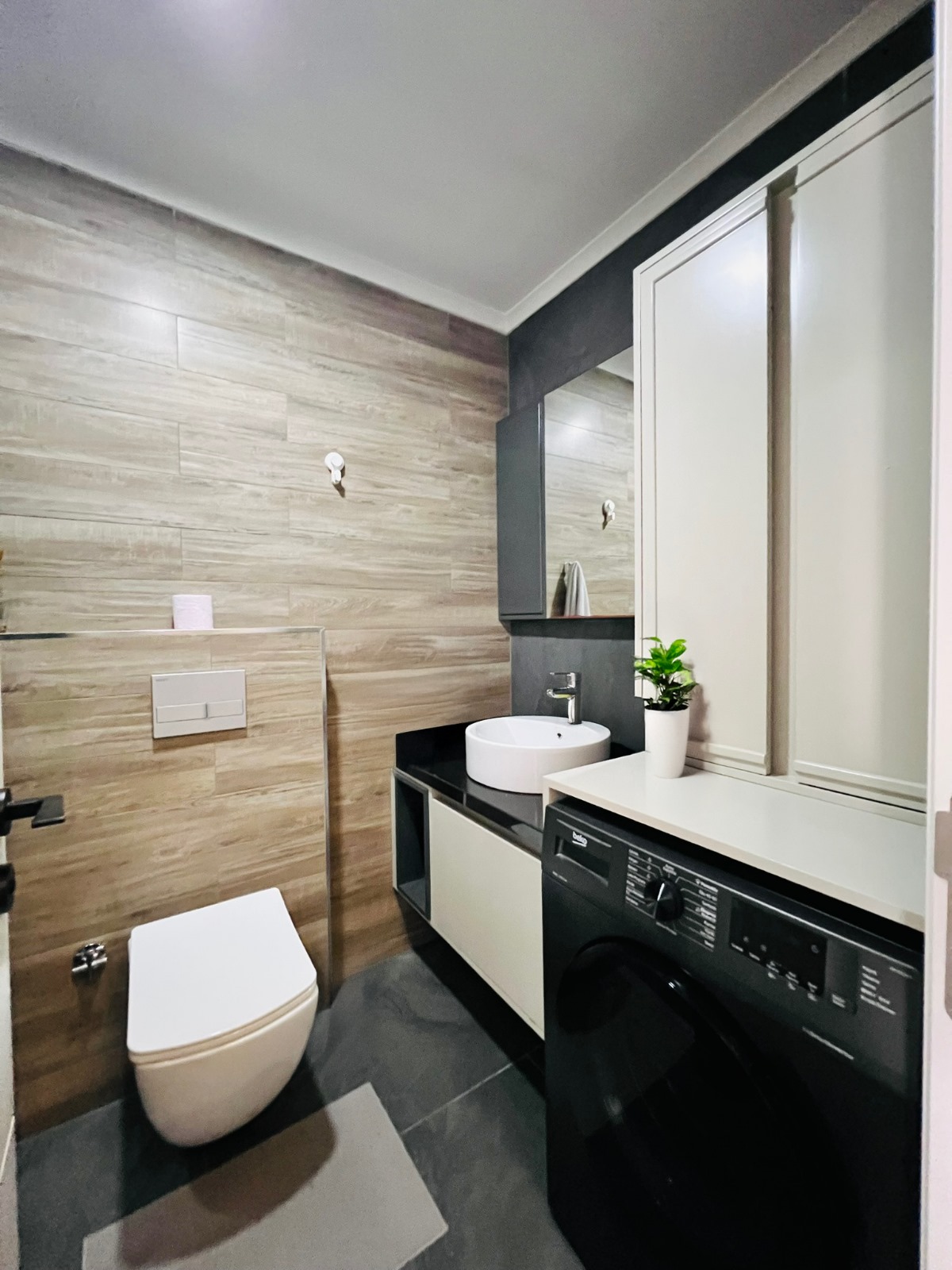 Ahşap görünümlü duvarlı banyo, yuvarlak lavabo ve asma klozet Mahmutlar’daki rezidansta