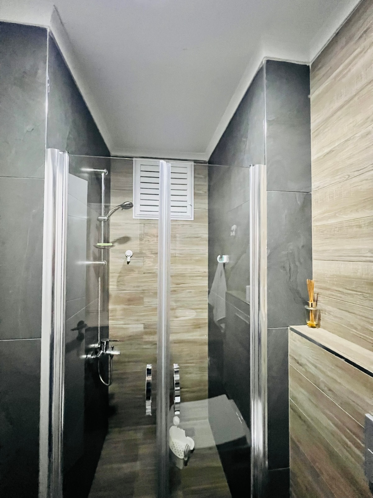 Cam duş kabinli banyo, ahşap dolaplı lavabo ve koyu zemin döşemesi penthouse içinde