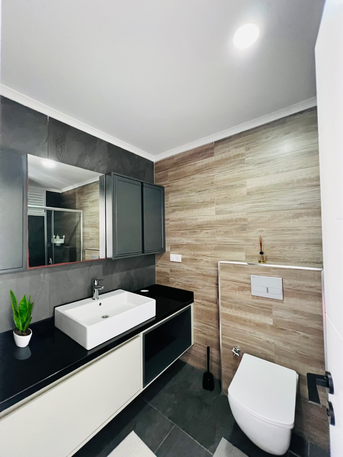 Duvara asılı lavabo, boydan boya ayna ve koyu zeminli banyo çatı katı dairede