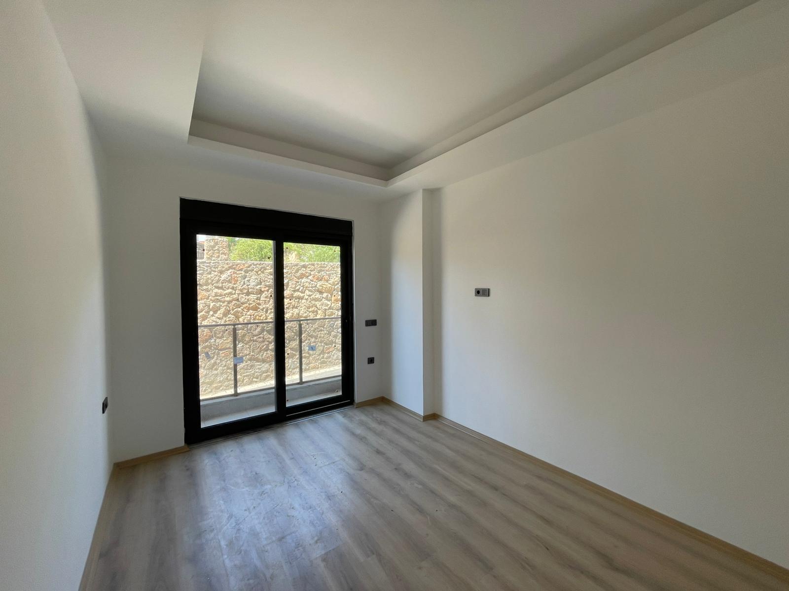 Açık ahşap görünümlü laminantlı yatak odası, Oba'da 2+1 konutta balkona açılan panoramik kapıyla