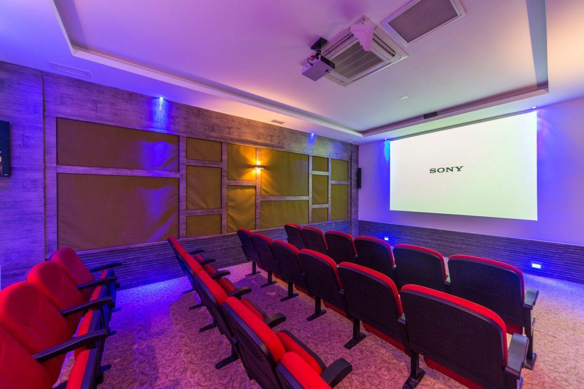Kırmızı koltuklu sinema salonunda büyük perde ve mor mavi aydınlatma