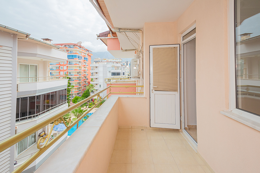 Uzun dar balkon altın renkli korkuluklarıyla Mahmutlar'da havuzlu dubleks daireye bakıyor