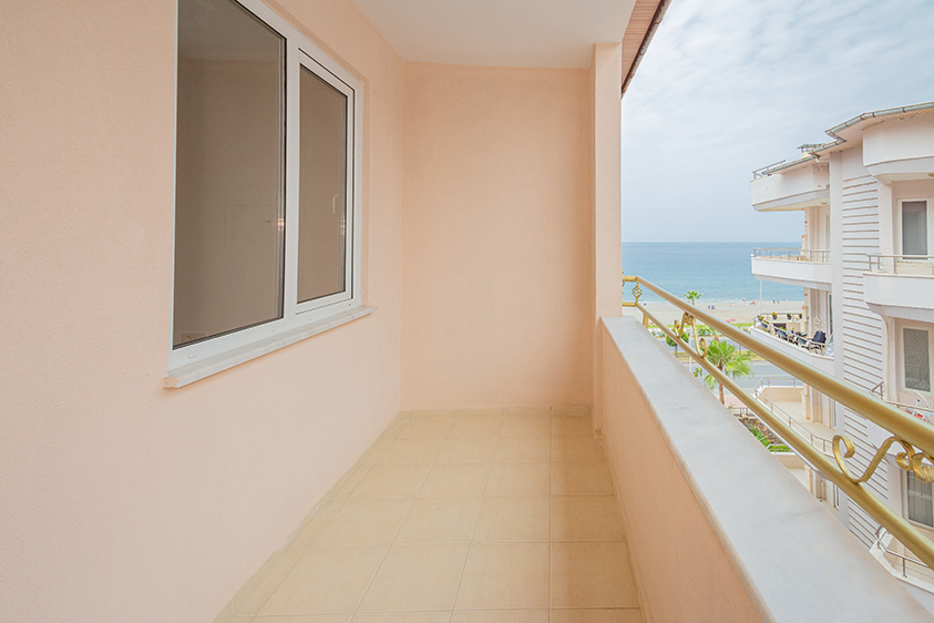 Dar balkon altın renkli korkuluklarıyla binalar arasından denizi gören dubleks dairede