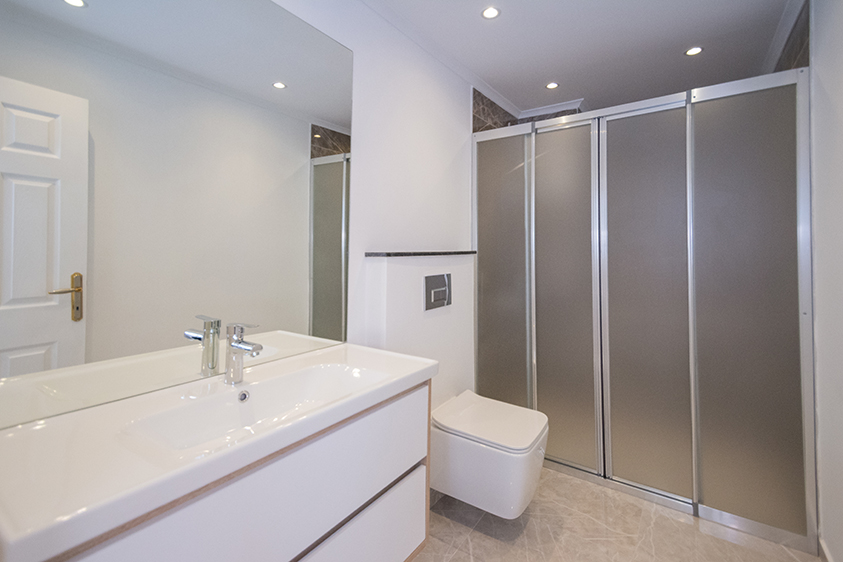 Asma lavabolu banyo büyük ayna ve mat cam duş kabiniyle sade iç mekânda yer alıyor