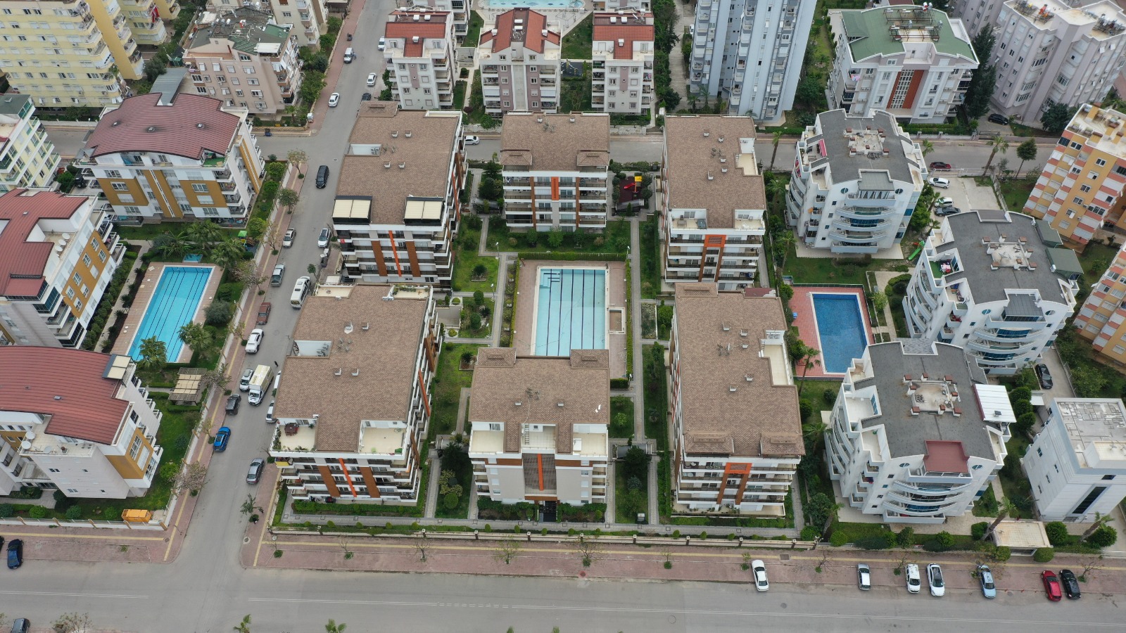 Вид сверху на комплекс с тремя бассейнами и зелёными дорожками, где продаются квартиры в Коньяалты
