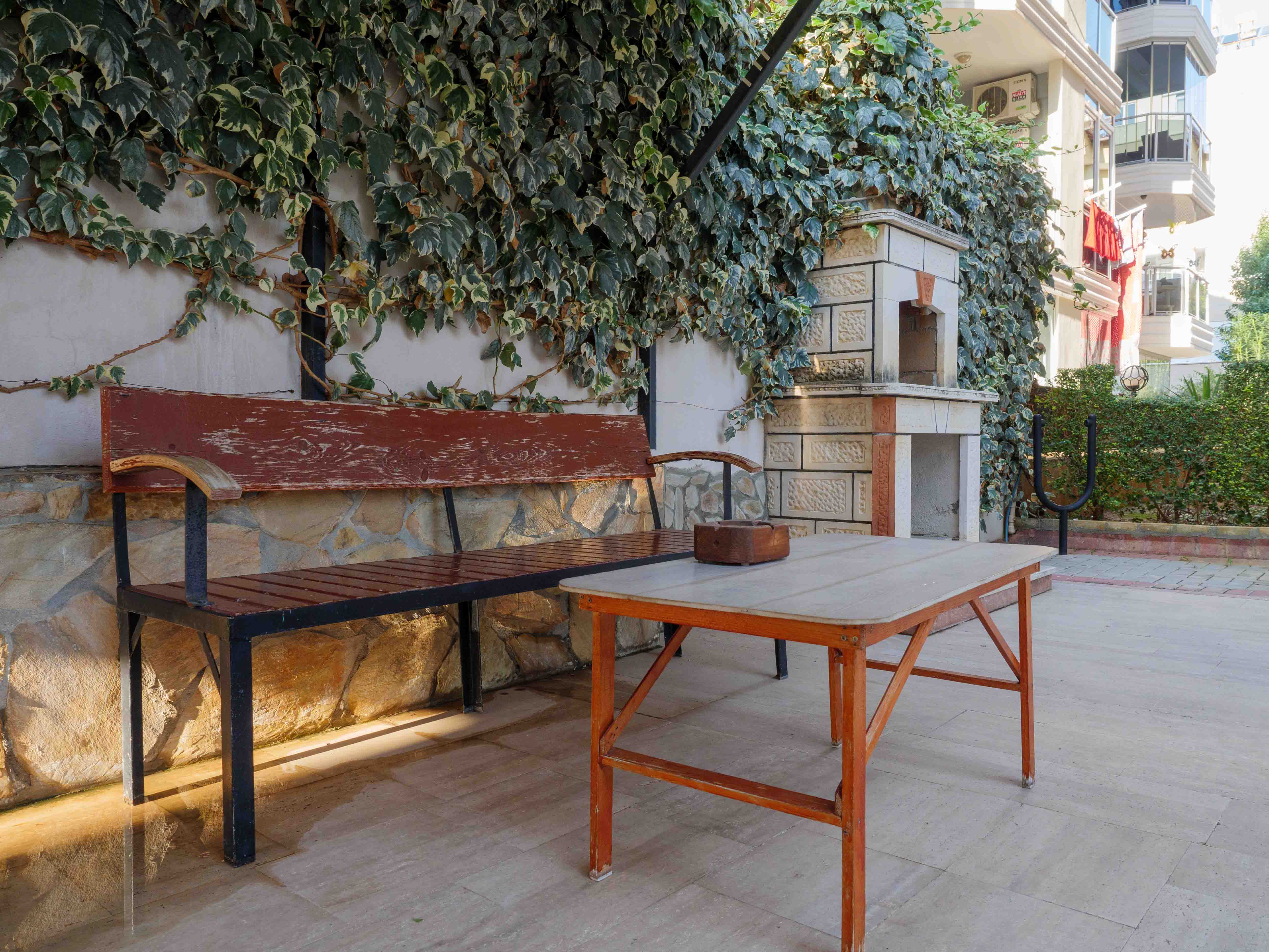 Ahşap masa ve bankın yanındaki taş dış mekân ocağı Oba’da satılık penthouse için