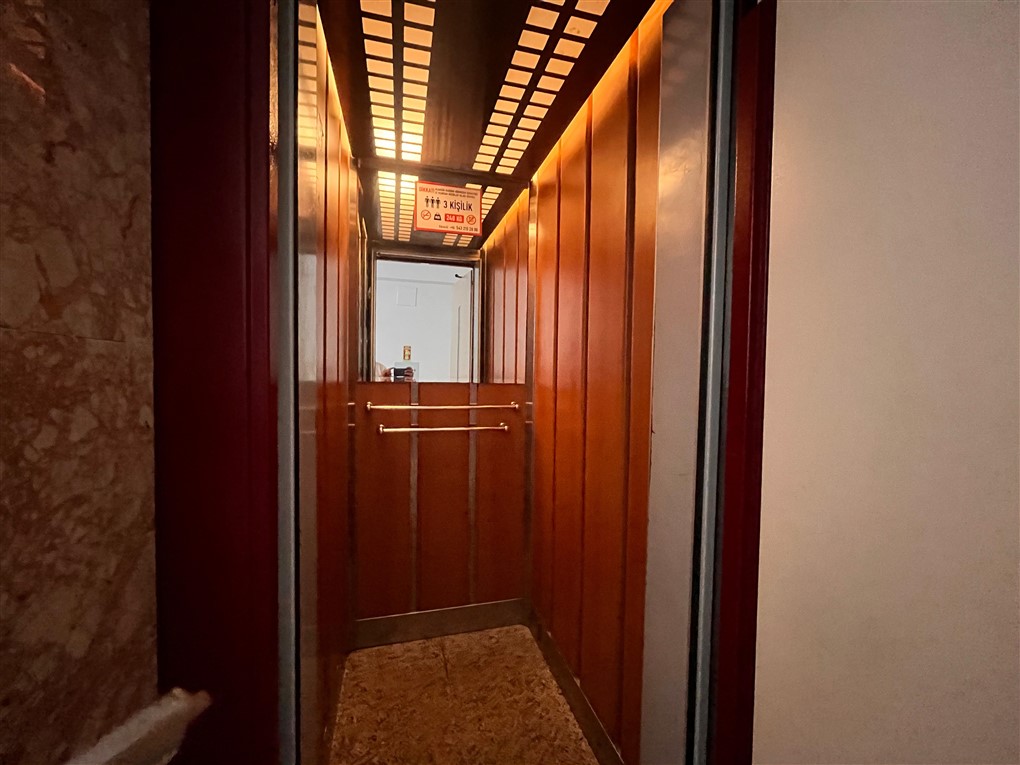 Ahşap panelli asansör kabini ve aynalı arka duvar Oba’daki çatı katı dairede