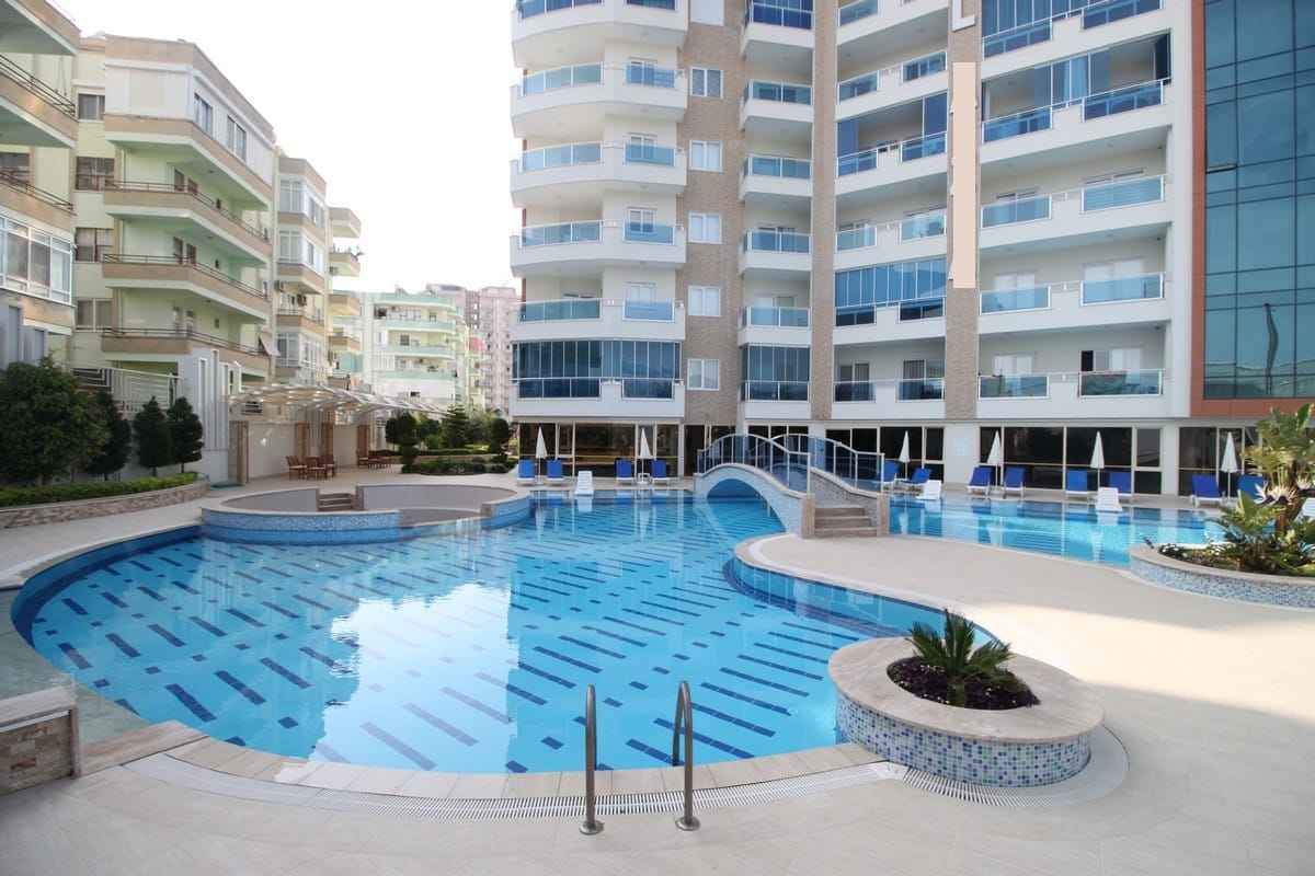 Open irregular pool with a bridge and palms at the development listed for sale