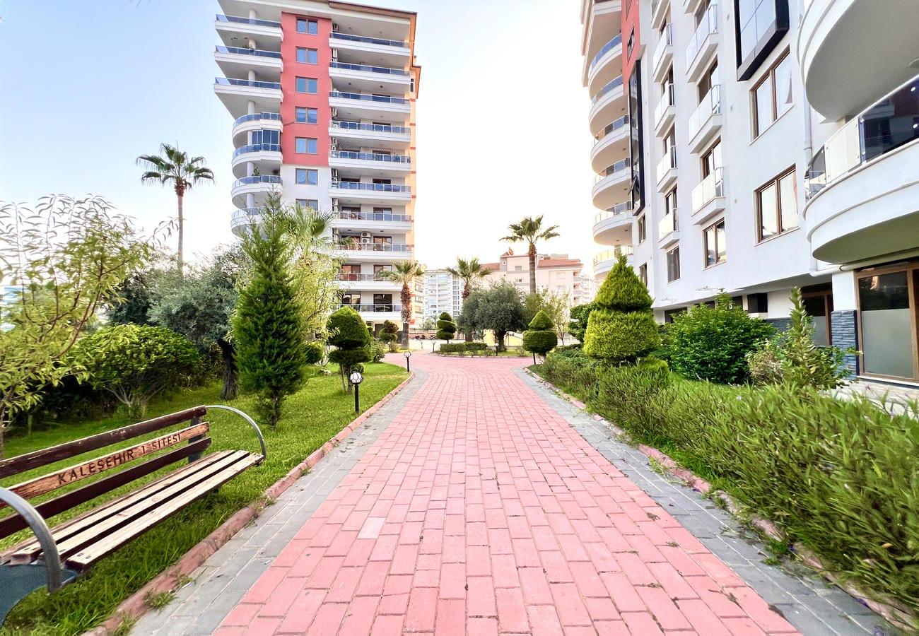 Pembe tuğla yol, çim ve palmiyeler satılık konutların bulunduğu sitenin düzenli bahçesinde