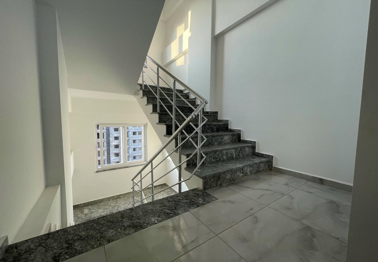 Interior staircase with dark stone steps, metal handrail and a window on the landing
