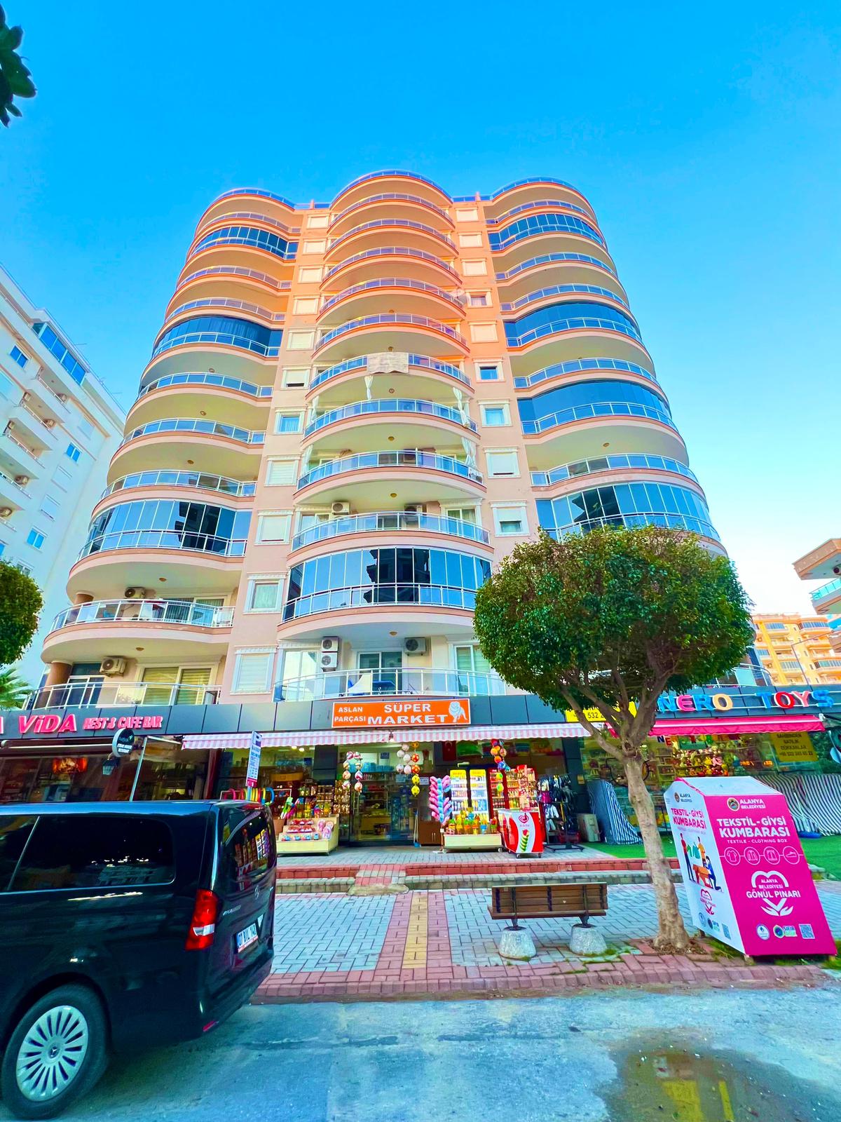 Cam balkon sıralı yüksek bina ve mağazalar, Türkiye’de satılık konutun şehir sokağını gösteriyor
