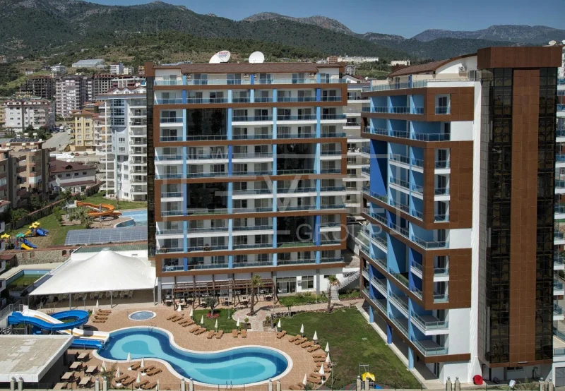 Glass balconies and a shaped pool frame a 1+1 apartment for sale in Cikcilli, Alanya, Turkey — New Level Group