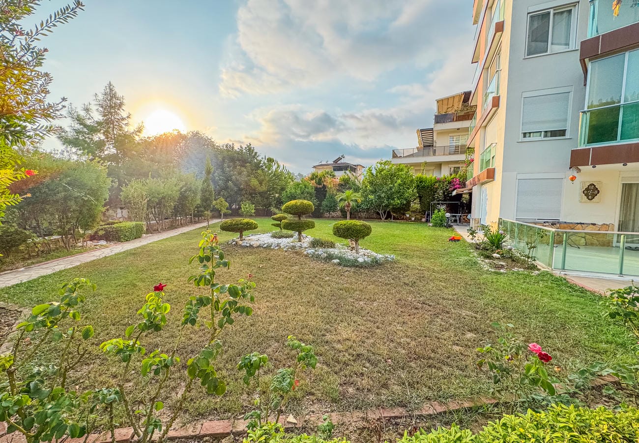 Çiçek açmış güllerin yanındaki bakımlı çim ve bahçe yolu, penthouse sakinlerinin kullandığı alanda