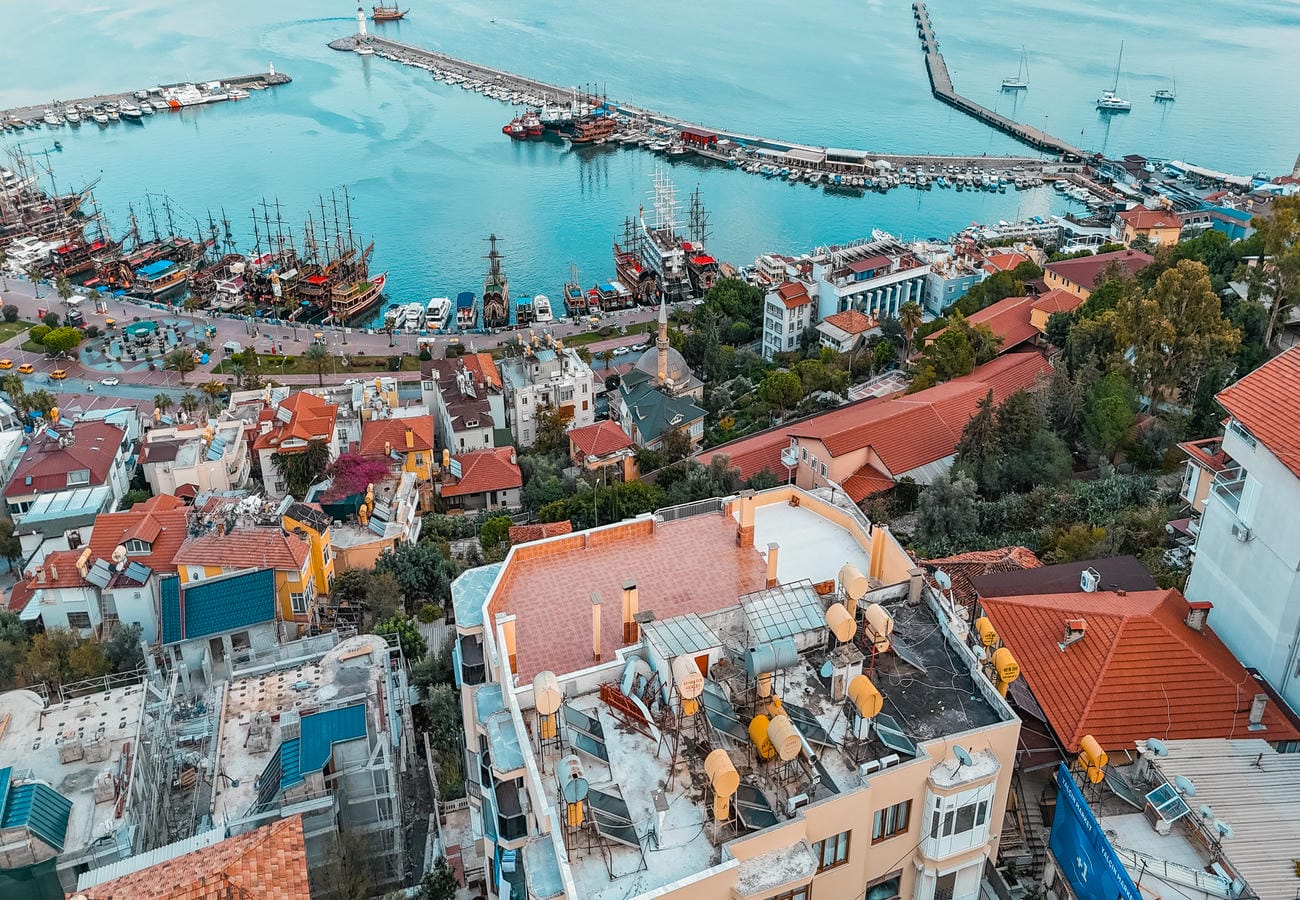 Port with long piers and turquoise water stretches across an aerial view of Alanya for sale