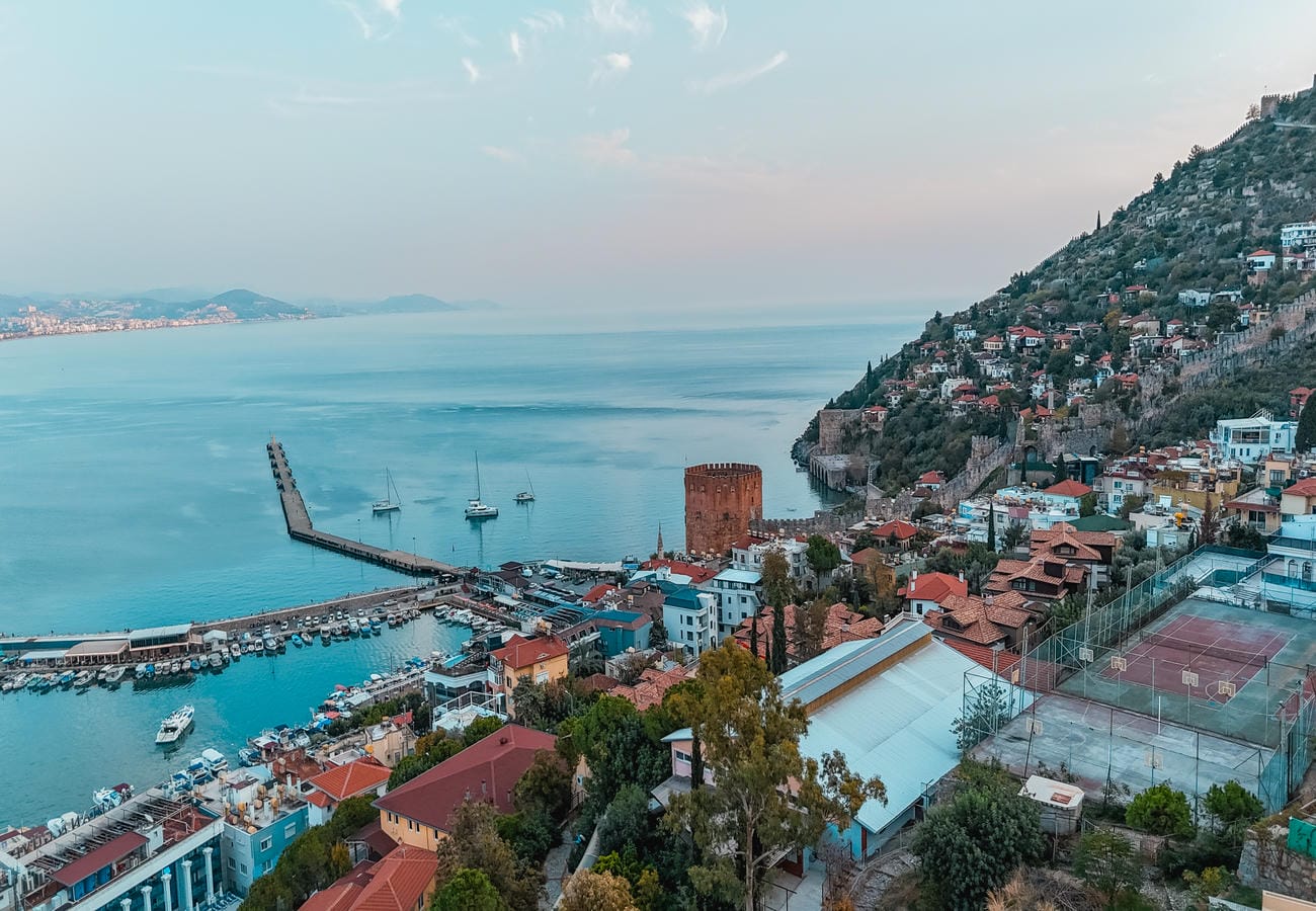 Sea bay with a red harbor tower and hillside homes shows a residence in Alanya, Türkiye