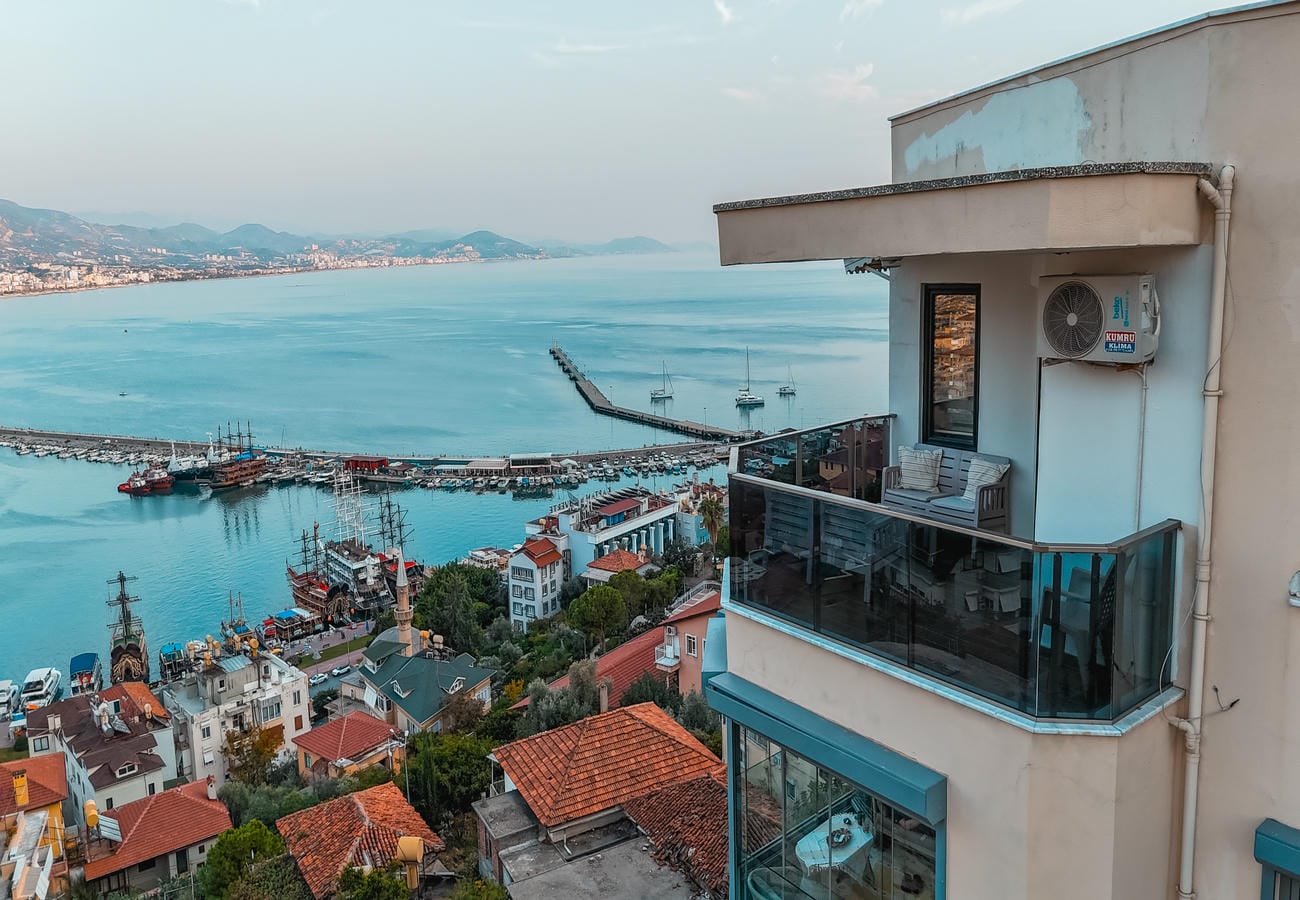 Balcony with glass railing and plastic furniture overlooks a bay and port in Alanya, Türkiye