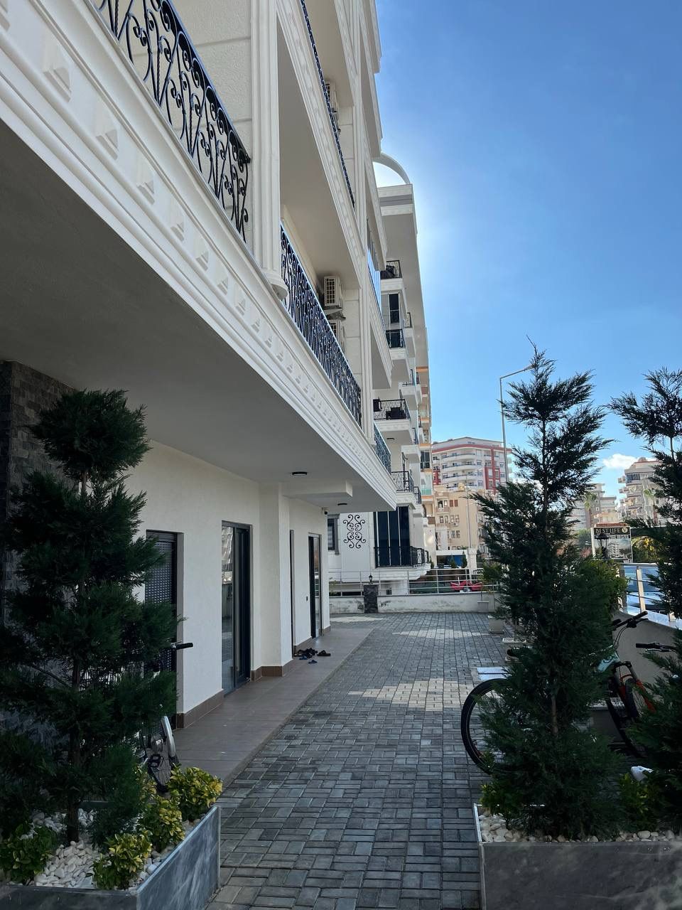 Paved walkway by a white facade with wrought-iron balconies in a complex with top-floor apartments for sale in Turkey