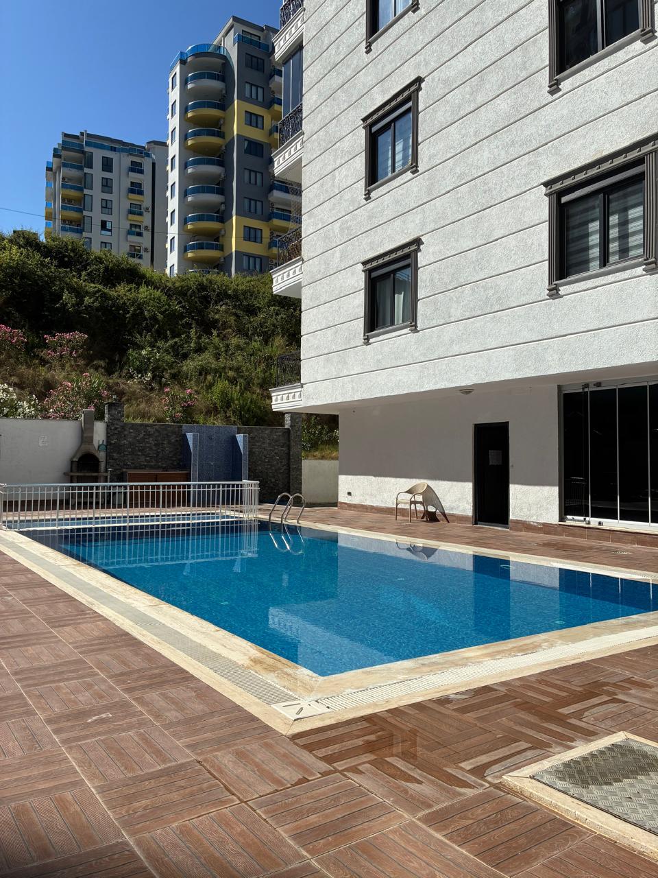 Outdoor pool with a blue mosaic lining beside a white facade at a residence in Turkey where apartments are for sale