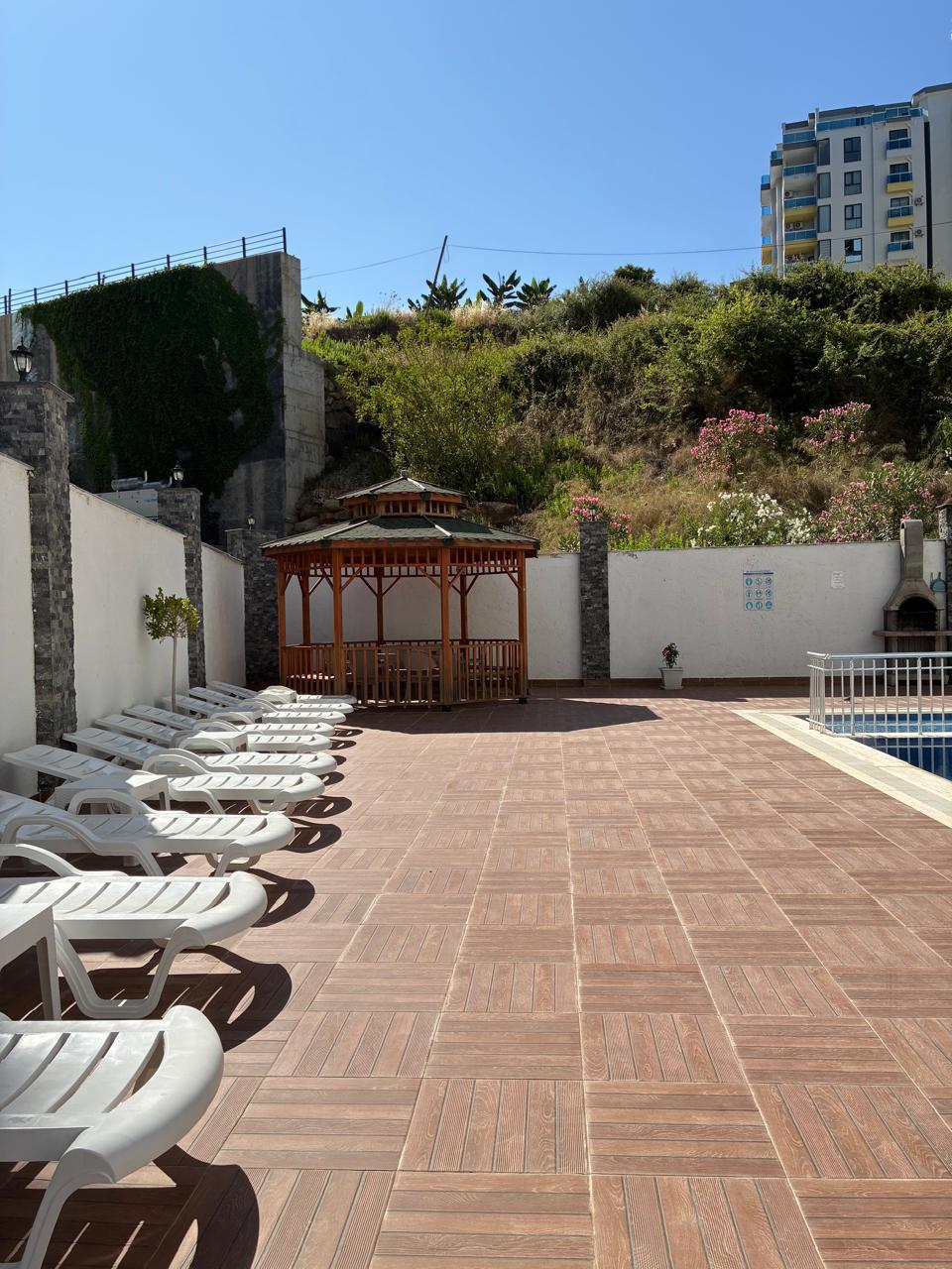 Row of white loungers by the pool and a wooden gazebo for residents of apartments in Turkey where homes are for sale