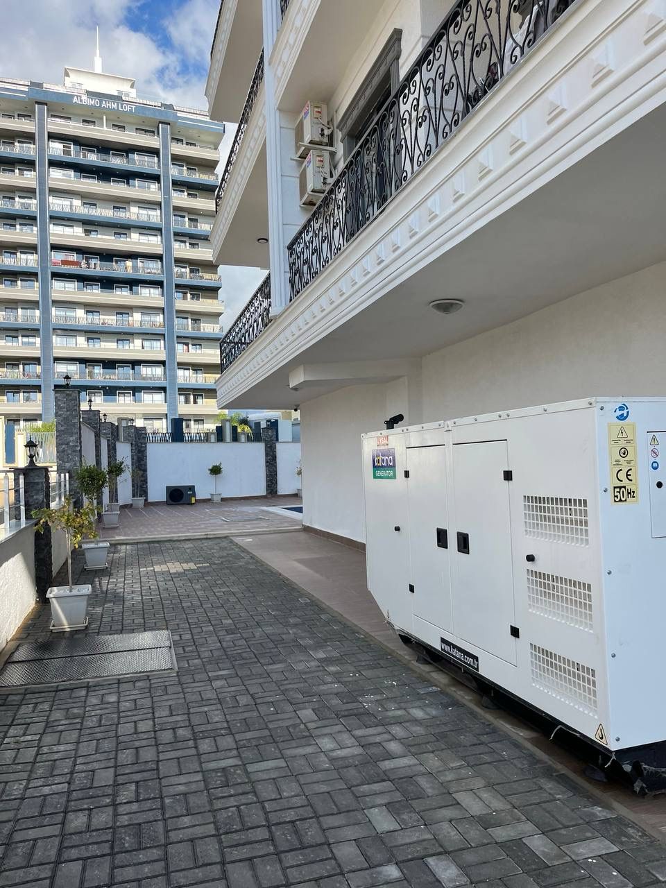 White diesel generator in the technical area of a complex with apartments beside a facade with balconies