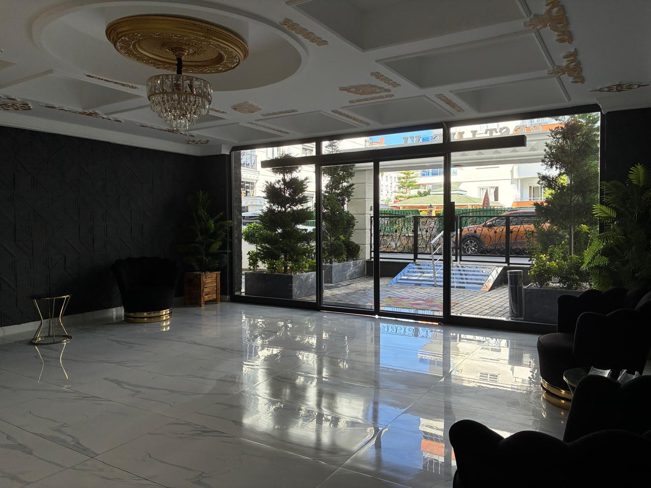 Lobby with a wide glass entrance, black patterned accent wall and armchairs with gold-toned bases