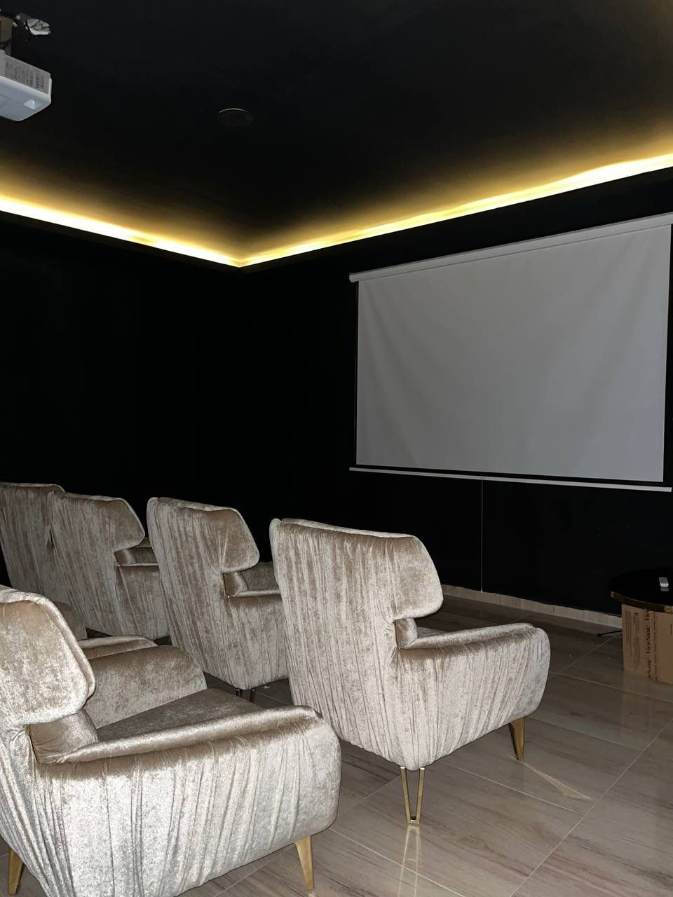 Cinema room with grey upholstered seats, a white projection screen and ceiling accent lighting in a complex with residences
