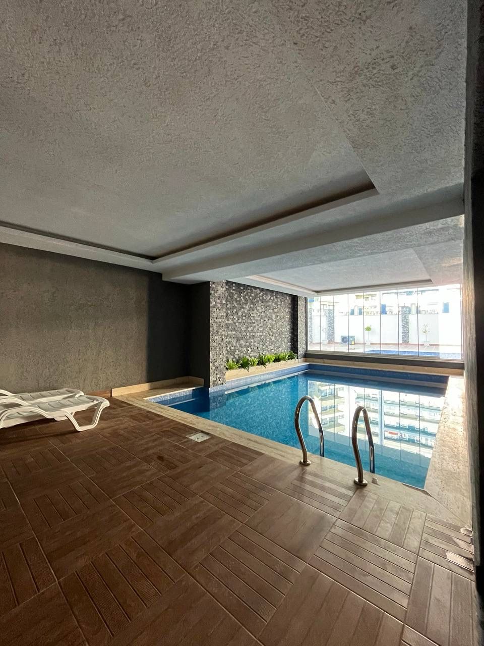 Indoor pool with wooden flooring by the water and panoramic windows in Alanya