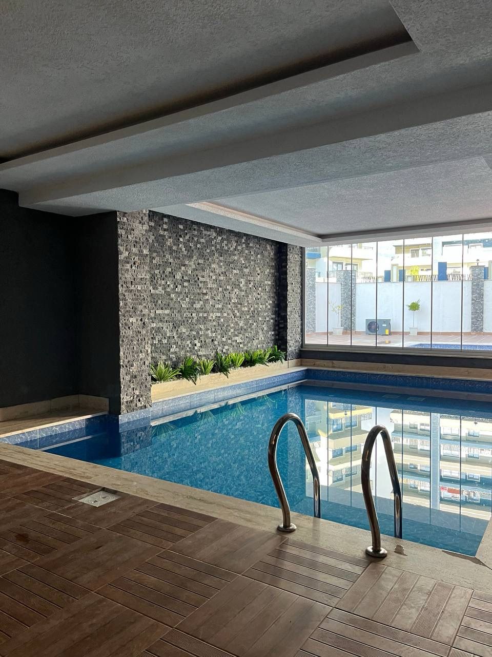 Blue indoor pool with twin metal ladders and a mosaic stone wall for residents of top-floor apartments