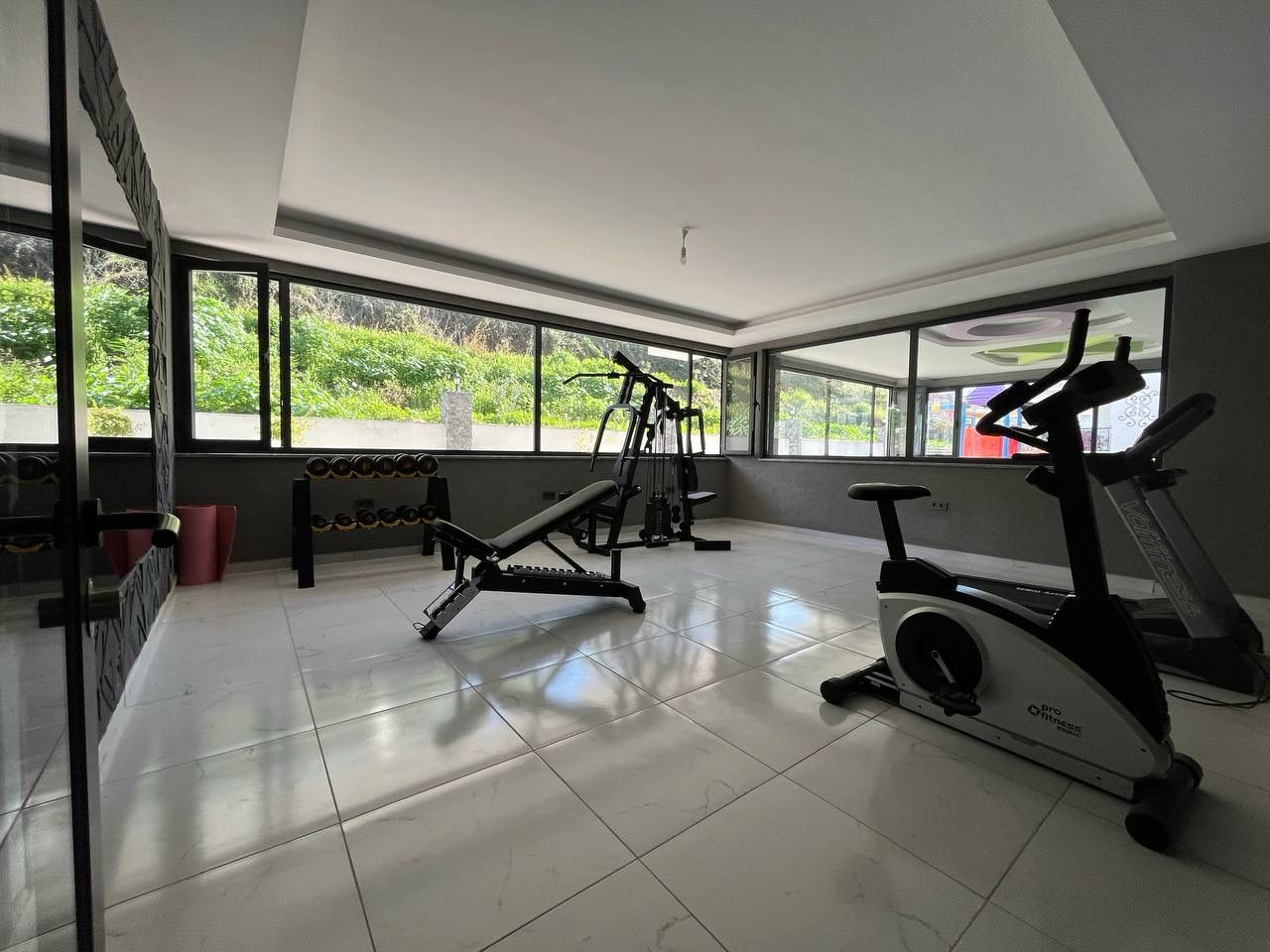 Gym with a treadmill, exercise bike and mirrored wall beside panoramic windows