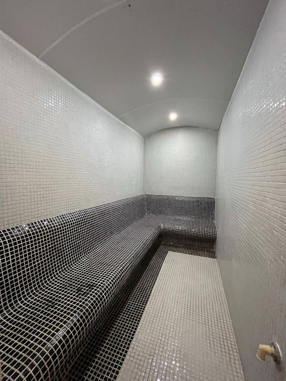 Steam room with a long mosaic bench and vaulted ceiling lighting for residents of a residence