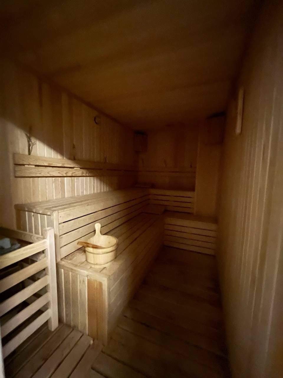 Sauna with tiered wooden benches, a bucket and warm subdued lighting in Mahmutlar