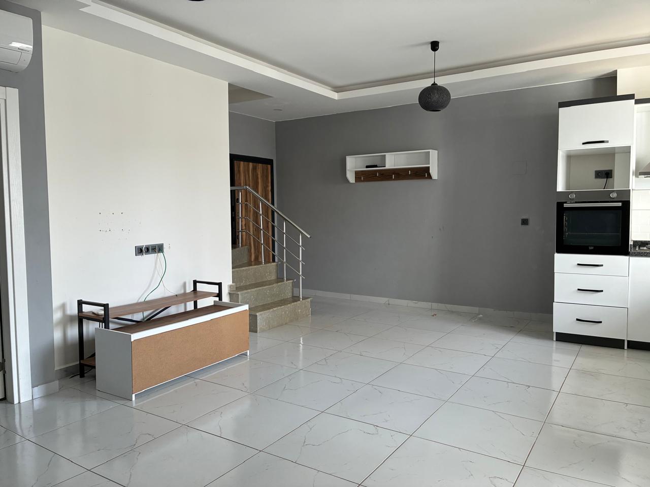 Kitchen-living room with a white corner kitchen and staircase in a 2+1 penthouse for sale in Turkey
