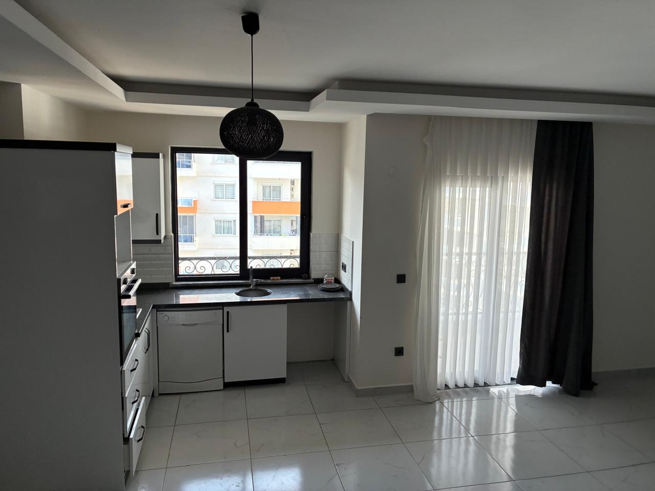 Kitchen-living room with white cabinetry, a black countertop and balcony door in a duplex in Alanya
