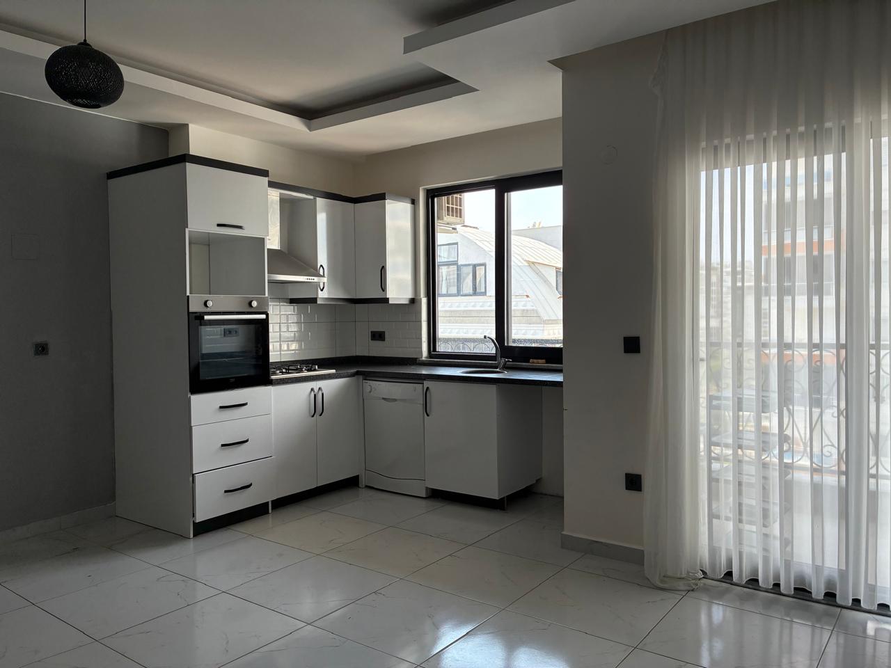 Corner kitchen with white cabinetry, black countertop and a balcony door in a top-floor apartment in Mahmutlar