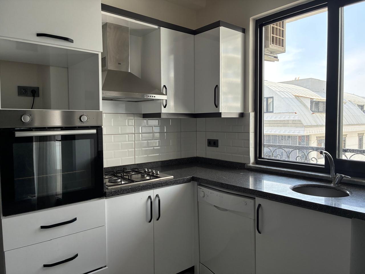 Kitchen with white cabinets, a granite countertop and round sink by the window in a top-floor apartment