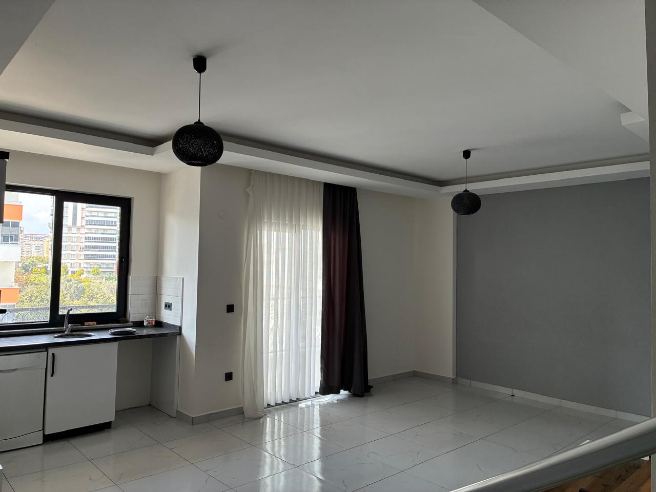 Empty kitchen-living room with a grey accent wall and balcony door in a residence in Türkiye